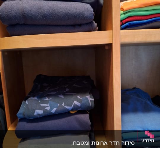 בגדים מקופלים בארון עץ, מסודרים לפי צבעים